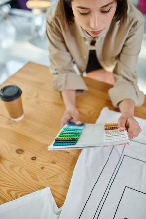 young asian designer looking at color palette while working near coffee to go in print studio