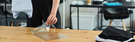 cropped view of woman packing neatly folded clothes in plastic bag on table in print atelier, bannerの写真素材