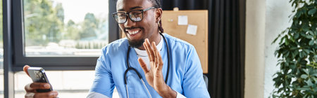jolly african american doctor with glasses waving at phone camera and smiling joyfully, bannerの写真素材