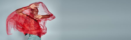 young african american man with red tulle fabric looking at camera, fashion concept, bannerの写真素材