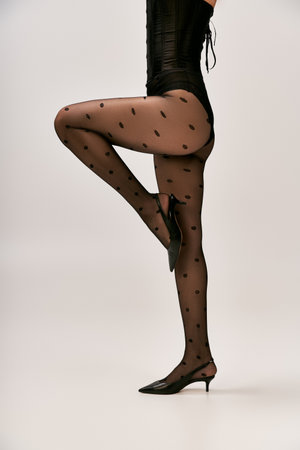 cropped shot of chic woman in corset, polka dot tights and high heels posing on white backdropの写真素材
