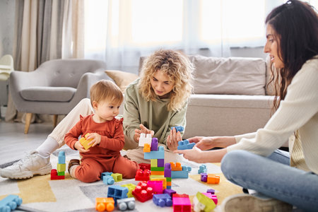 joyous lesbian couple playing with their baby girl with toys on floor at home, family conceptの写真素材