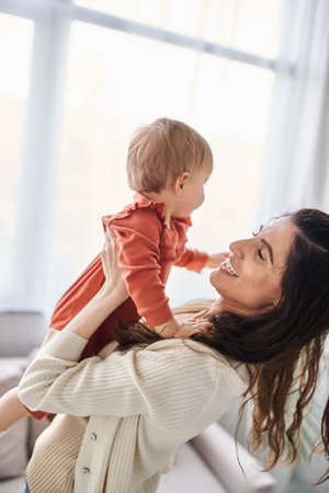 beautiful happy woman in cozy homewear playing actively with her baby daughter, family conceptの写真素材