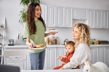 attractive blonde woman preparing pancakes for breakfast to her blurred baby girl, family conceptの写真素材