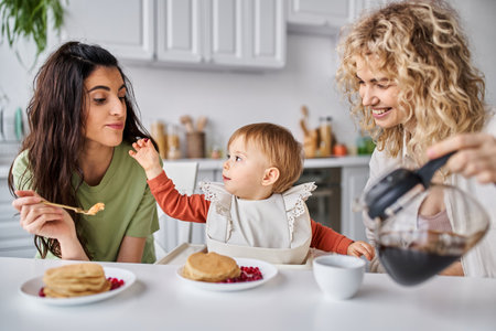 joyful beautiful lgbt couple having delicious breakfast with their baby girl, family conceptの写真素材