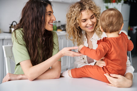attractive merry lesbian couple in homewear posing happily with their baby girl, modern parentingの写真素材