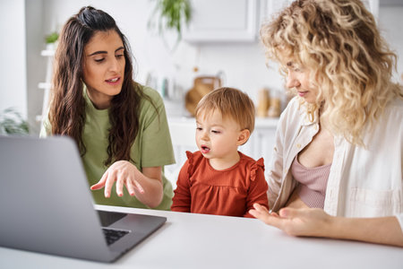 loving lgbt couple watching movies with their daughter on laptop on kitchen, modern parentingの写真素材