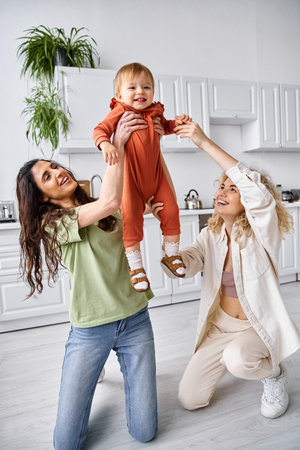charming happy lgbt couple playing actively with their cute toddler daughter, modern parentingの写真素材