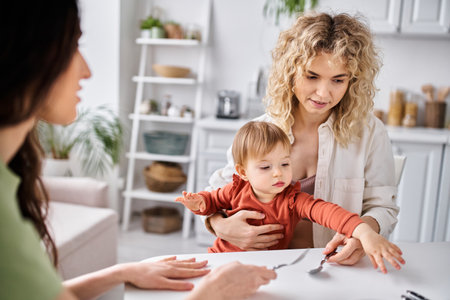 adorable baby girl surrounded by her attractive mothers that holding spoons, family conceptの写真素材