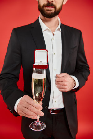cropped view of man in black suit with champagne glass and gift box with jewelry ring on redの写真素材
