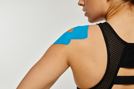 cropped view of young woman in black comfy sport wear with kinesiological tapes on her shoulderの写真素材