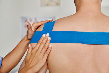 cropped view of hand of young female doctor putting kinesio tape on shoulder of her patientの写真素材