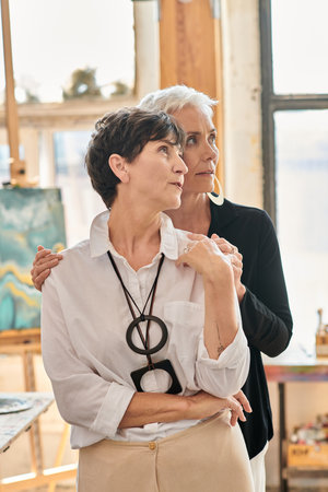 thoughtful and stylish lesbian artists looking away in modern art studio with creative paintingsの写真素材