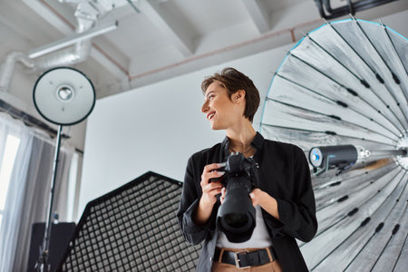 cheerful female photographer in casual clothes with camera in her hands smiling and looking away