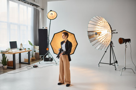 attractive young female photographer in everyday outfit posing in her studio and looking away