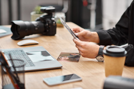 cropped view of camera and coffee on table next to young female photographer with photos in handsの写真素材