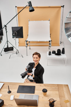 cheerful professional woman in casual attire smiling at camera working at her workplace in studioの写真素材