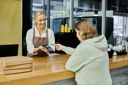 young woman with down syndrome paying with credit card near administrator with terminal in cafe