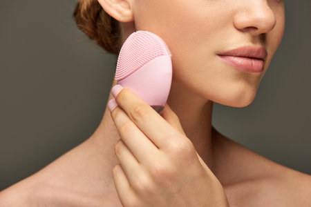 cropped woman holding cleansing brush on grey background, beauty gadget and skin care conceptの写真素材