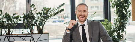 portrait of successful elegant businessman in grey suit smiling at camera in modern office, banner