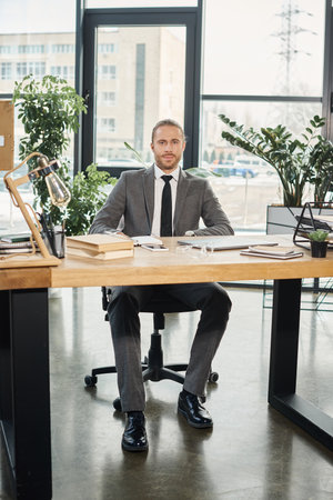 confident businessman sitting at work desk with documents and digital devices in modern officeの写真素材