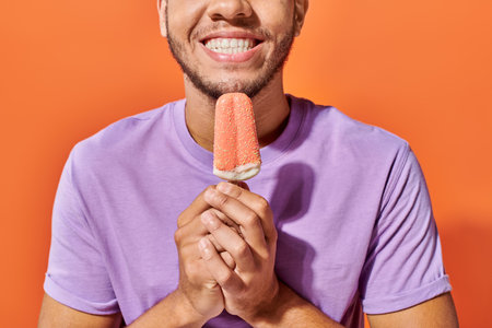 cropped shot of african american man holding ice cream with sprinkles on orange background