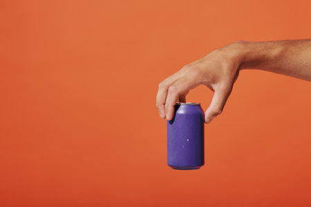 cropped view of person holding purple soda can in hand on orange background, carbonated drinkの写真素材