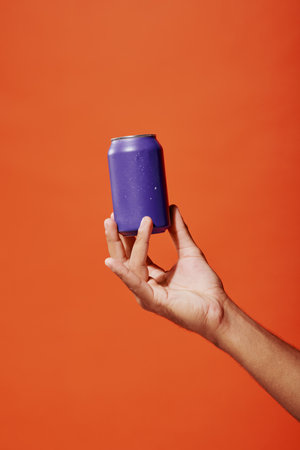 cropped shot of person holding purple soda can in hand on orange background, carbonated drinkの写真素材