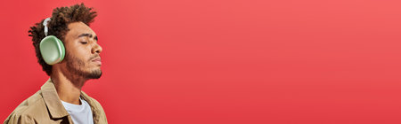 young african american man in wireless headphones listening music on red background, banner