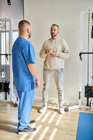 handsome man discussing treatment plan with doctor in blue uniform in recovery kinesio center