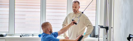 young physiotherapist training on exercise machine, instruction of man in kinesio center, banner