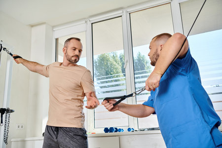 medical assistant in blue uniform preparing man for training on exercise machine in kinesio center