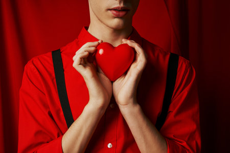 cropped view of young man holding small heart in his hands on red background, Valentines day conceptの写真素材