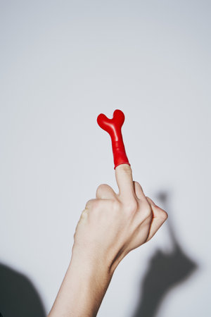 cropped view of provocative young man showing middle finger with red balloon on grey background