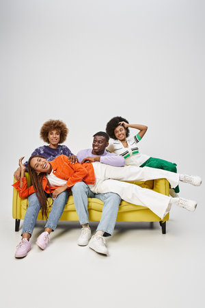 positive african american woman with dreadlocks lying on laps of friends sitting on yellow couch