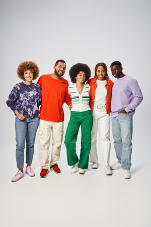 happy african american woman hugging her friends in vibrant attire on grey background, Juneteenth