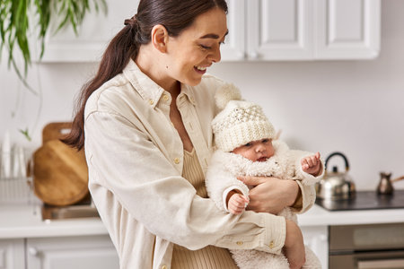 beautiful joyous woman in cozy homewear posing with her cute newborn baby boy, modern parenting