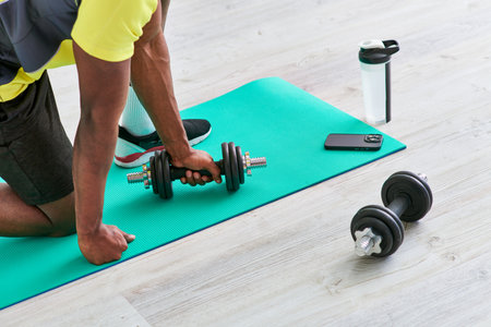 cropped african american man in sportswear working out with dumbbell on fitness mat at homeの写真素材