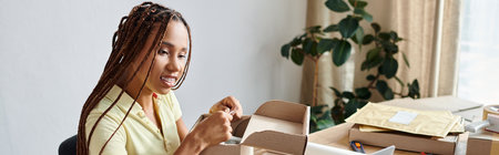 cheerful african american female seller packing box and looking at laptop, delivery concept, bannerの写真素材