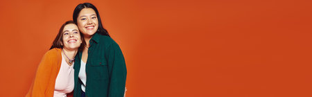 radiant and multicultural female friends sharing a joyous moment on warm orange backdrop, bannerの写真素材