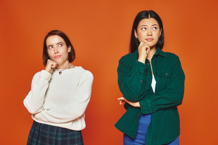 pensive young multicultural friends in vibrant attire looking away on orange background, thinkの写真素材