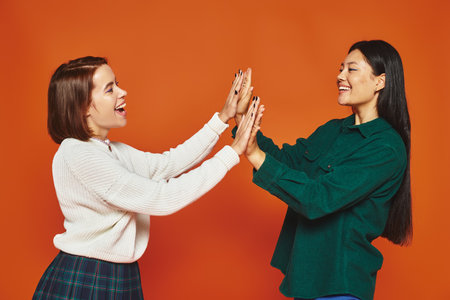 happy young multicultural friends in vibrant attire giving high five on orange backgroundの写真素材