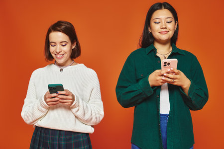 multicultural women using smartphones, engaged in social media on vibrant orange backgroundの写真素材