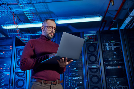good looking hardworking data center specialist in turtleneck looking at his laptop attentively