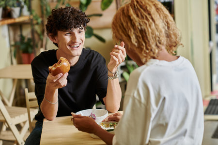 smiling and curly man eating tofu burger near african american girl enjoying salad in vegan cafeの写真素材