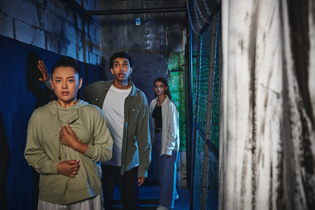 young and interracial friends walking through secret passage in quest room, adventure and mystery
