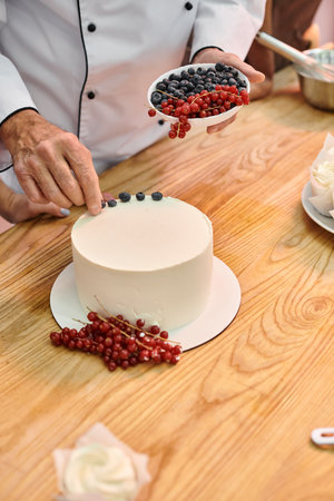 cropped view of mature chef showing his student how to decorate cake with berries, cooking coursesの写真素材