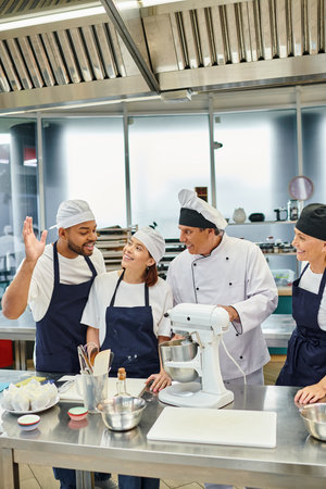 jolly african american chef raising hand to ask question next to his colleagues and chief cookの写真素材