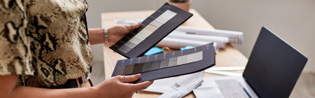 cropped view of woman stylist with color samples near laptop with blank screen in atelier, banner