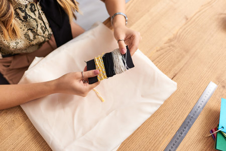 cropped view of dressmaker holding threads near fabric and sewing supplies in personal atelier